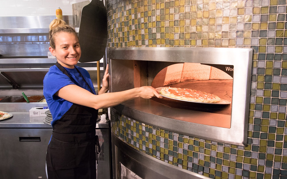 Student worker putting a pizza in an oven